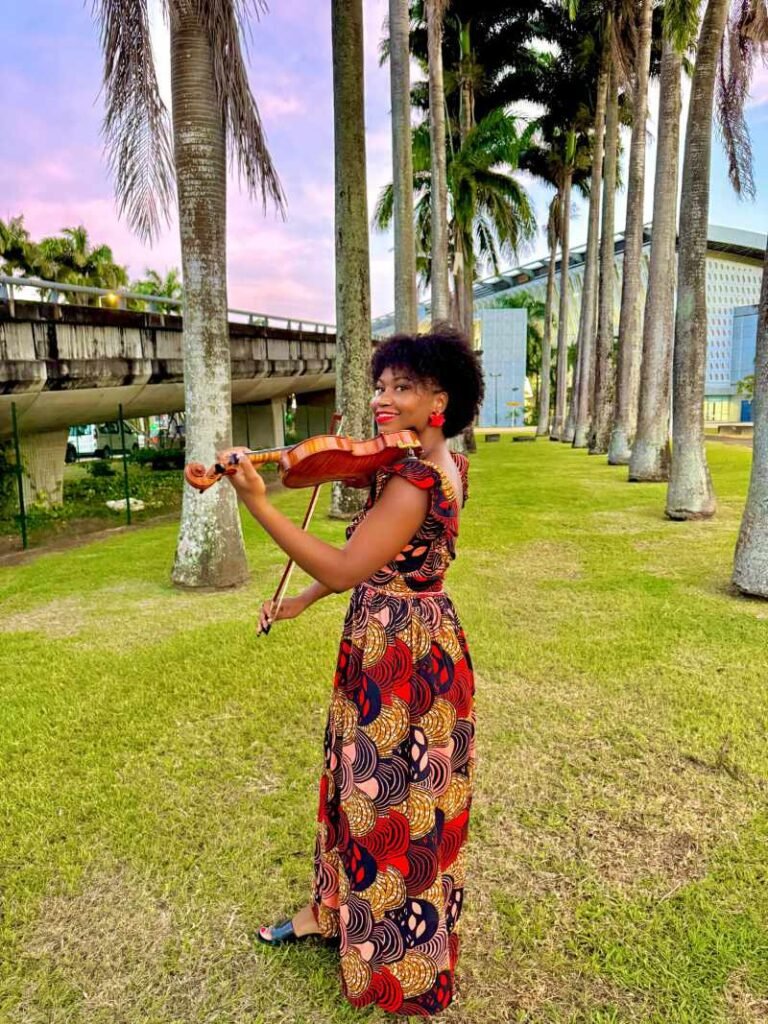 Fanélie Nebor, violoniste, jouant du violon en plein air en Guadeloupe, vêtue d'une robe colorée aux motifs créoles